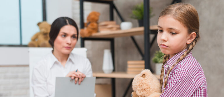 A girl holding a teddy bear looks upset with her mother sitted right in the front of a girl