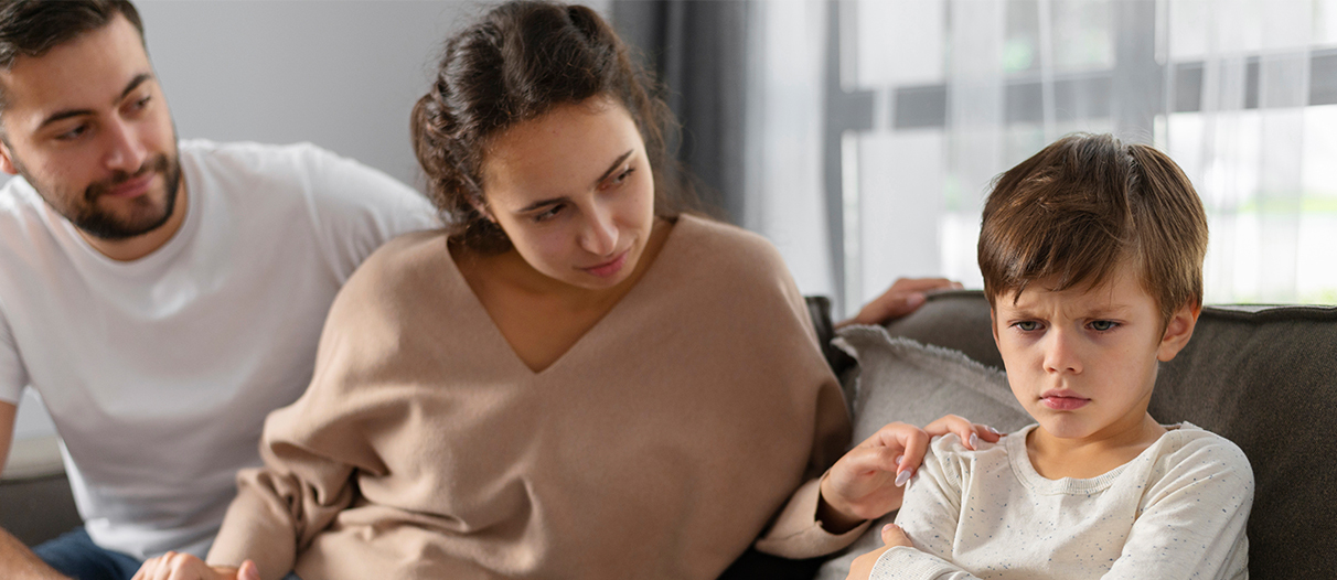 A boy sitting on the couch along with his parents and seems the boy is upset